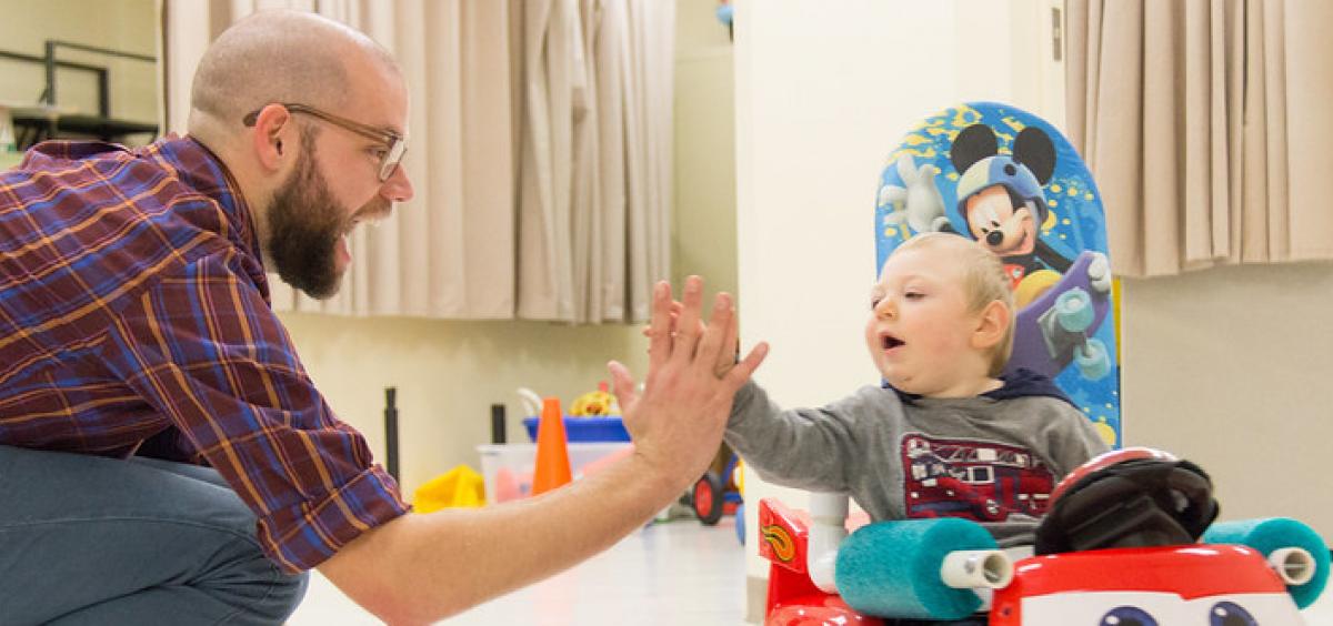 Researcher Sam Logan high-fives a child using a Go Baby Go car
