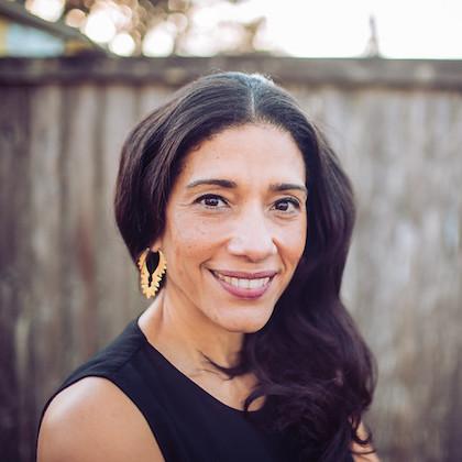 Headshot of OSU professor Ana Spalding, where she is smiling at the camera, wearing a black top and gold earrings.