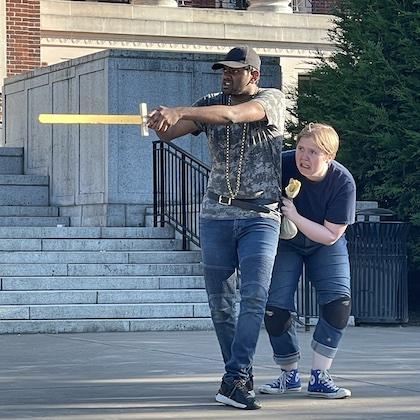 Photo from Comedy of Errors rehearsal shows Srimanyu Ganapathineedi as Antipholus of Syracuse, brandishing a sword, and Sophie Brown as Dromio of Syracuse, cowering behind