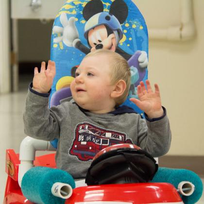 A child raises both hands in the air while sitting in a Go Baby Go car