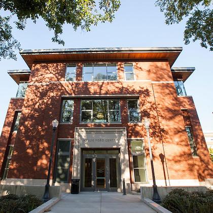Image of the front of the Hallie E. Ford Center, looking up, as bright sunlight filters through the trees.