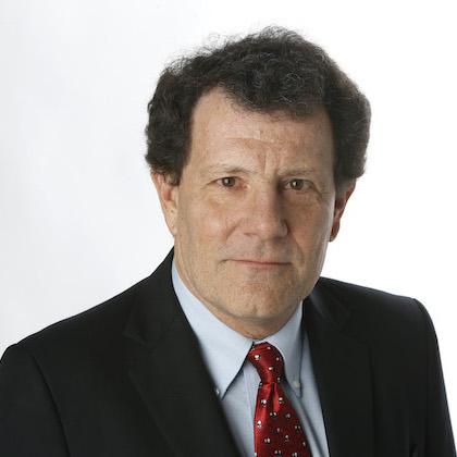 Image shows a headshot of Nicholas Kristof, 63-year-old white man with dark brown hair, wearing a black suit jacket, light blue button-down shirt and red tie.