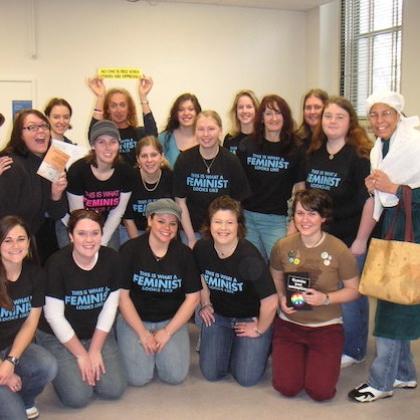 A group of students from the Women, Gender, and Sexuality Studies program stand close together and smile for a picture while wearing bright blue t-shirts that say "This is what a feminist looks like."